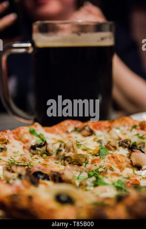 Pizza au fromage fondu de fruits de mer et des herbes saupoudré sur le dessus et une grande tasse de la bière. Banque D'Images
