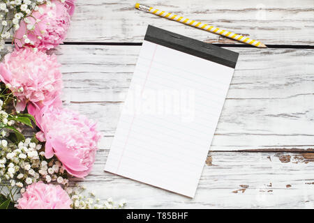 Les Pivoines roses et gypsophile fleurs avec pensil et vide remarque livre blanc sur une table en bois rustique avec arrière-plan copie de l'espace pour votre texte. Télévision Banque D'Images