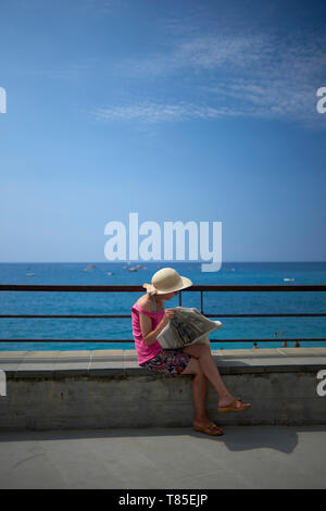 Femme Asiatique portant un grand chapeau de paille lire un journal assis et profiter de la ville en bord de mer dans la région de Cinque Terre Italie en soleil Banque D'Images