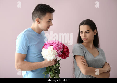 Jeune femme offensée refusant de prendre des fleurs de son petit ami sur un fond de couleur Banque D'Images