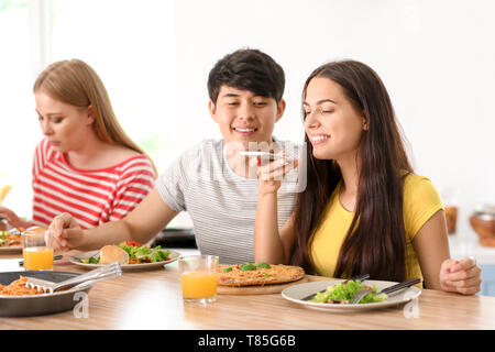 Young woman taking photo de nourriture alors qu'il était assis à table avec des amis dans la cuisine Banque D'Images