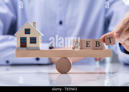 Close-up of Businessman's Hand Putting mot la dette sur l'équilibrage de la balançoire en bois Model House Banque D'Images