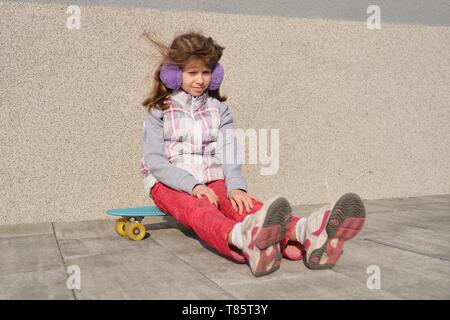 Petite fille monte un skateboard, dans la zone près de la maison, la saison du printemps, fond de mur gris. Banque D'Images