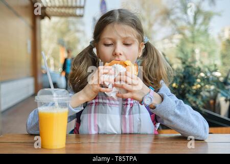 Portrait de jeune fille étudiant avec sac à dos, manger burger avec du jus d'orange, l'arrière-plan de restauration rapide en plein air cafe. Banque D'Images