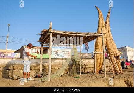 Filets de fixation pêcheur à côté de Caballitos de Totora (embarcations traditionnelles faites de roseau et utilisé pour la pêche et le surf) sur Huanchaco plage, Pérou Banque D'Images