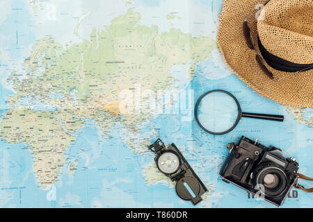 Vue de dessus du chapeau de paille, boussole, loupe et appareil photo sur carte du monde Banque D'Images