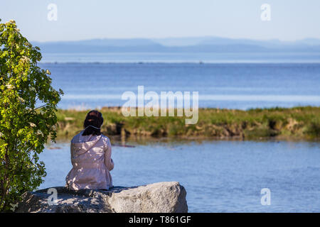 Jeune fille assise sur un rocher à l'ombre d'un arbre à l'échelle de l'île de Vancouver Banque D'Images