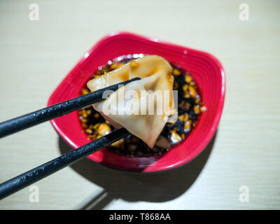 Dumpling chinois en baguettes trempées dans une sauce à l'ail soja Banque D'Images