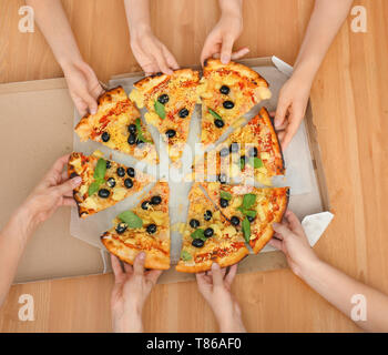 Les femmes prenant des tranches de pizza italienne de la case sur la table en bois, vue du dessus Banque D'Images