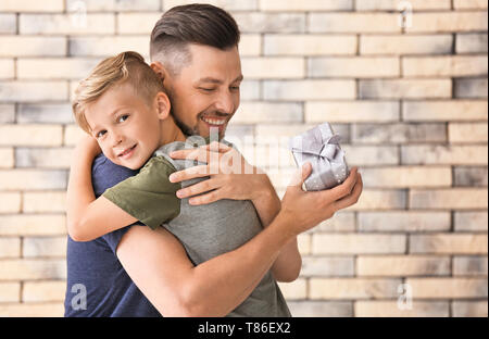 La réception de l'homme cadeau pour le jour de père de son fils sur fond brique Banque D'Images