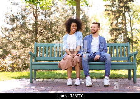 Jeune couple interracial aimant assis sur un banc de parc sur le printemps Banque D'Images