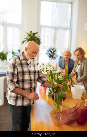 L'homme aux cheveux gris positif d'admirer de belles fleurs Banque D'Images