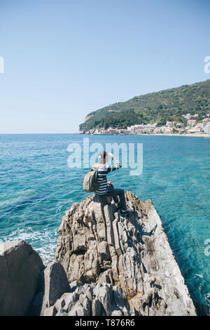 Un touriste avec un seul sac à dos se trouve sur une falaise au bord de la mer et se penche sur la distance à la vue de Petrovac, Monténégro. Banque D'Images