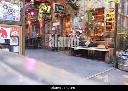 BUDAPEST, HONGRIE - avril 2019 : Intérieur de la célèbre ruine Jardin Szimpla pub avec femme assis sur un banc à jouer avec téléphone mobile. Banque D'Images