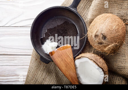 Coquille de noix de coco, avec de la viande, poêle en fonte et la spatule sur le chanvre sacs sur une table de cuisine en bois blanc Banque D'Images