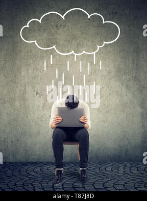 Triste portrait sur une chaise avec un ordinateur portable à la recherche vers le bas avec un nuage de pluie au-dessus Banque D'Images