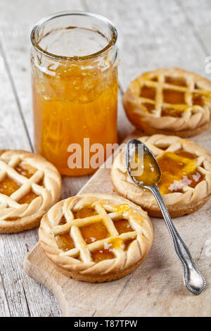 Tartes fraîchement cuit au four avec de la marmelade d'abricots et de remplissage dans un bocal en verre sur une planche à découper sur fond de table en bois rustique. Banque D'Images