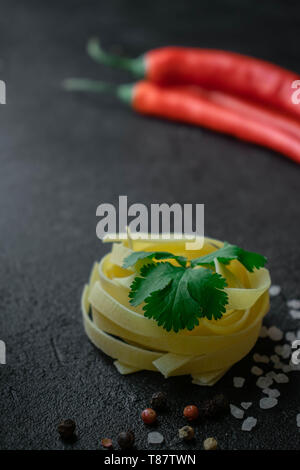 Sur un fond foncé matières fettuccine coller enveloppé dans une boule avec des feuilles de coriandre verte de gros sel de mer, poivre noir et rouge et son ensemble Banque D'Images