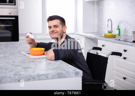 Smiling Mobilité jeune homme assis sur fauteuil roulant soupe potable dans la cuisine Banque D'Images