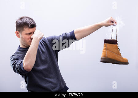 Portrait d'un homme portant sur son nez tout en maintenant ses chaussures puantes contre fond blanc Banque D'Images