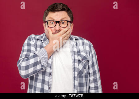 Portrait of middle aged man in casual chemise à carreaux et des lunettes debout, couvrant sa bouche et looking at camera avec peur f Banque D'Images