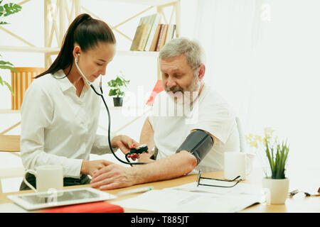 L'infirmière visiteuse ou visiteur santé prendre soin de man. Portrait de vie à la maison. La médecine, les soins de santé et la prévention. Fille de contrôler ou mesurer la pression artérielle du patient lors de la visite. Banque D'Images