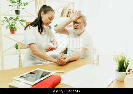 L'infirmière visiteuse ou visiteur santé prendre soin de man. Portrait de vie à la maison. La médecine, les soins de santé et la prévention. Fille de contrôler ou mesurer le pouls du sang du patient lors de la visite. Banque D'Images