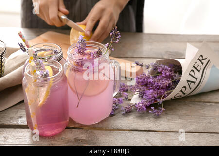Bocaux Mason avec de délicieuses boissons et de jeune femme la préparation de la limonade à la lavande à table Banque D'Images