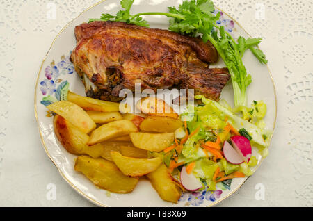 Assiette de porcelaine avec un grand morceau de rôti de porc et pommes de terre frites avec salade de choux, carottes et radis avec un brin de coriandre se situent sur une p blanc Banque D'Images