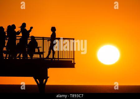 Pays de Galles Aberystwyth UK, le samedi 11 mai 2019 UK Weather : Les gens sont découpé sur le glorieux coucher de soleil puisqu'elles se tiennent sur la jetée de Aberystwyth, sur la côte de la Baie de Cardigan, l'ouest du pays de Galles. Le temps est réglé à se réchauffer de nouveau dans la semaine à venir après comme période d'instabilité des conditions froides. crédit photo Keith Morris / Alamy Live News Banque D'Images