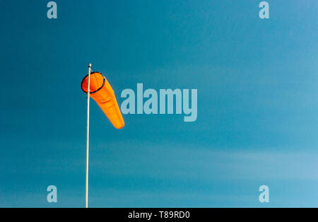 Plaine inclinée vers le bas de manche orange vif sur pôle blanc contre un ciel bleu clair. Banque D'Images