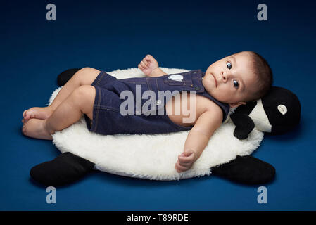 Petit bébé couché sur un oreiller isolé sur fond bleu studio Banque D'Images
