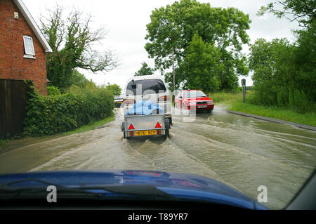 Conduite à travers la route inondée avec des voitures. Vue du conducteur de l'intérieur de la voiture conduite à travers l'inondation d'eau de pluie dans la route de campagne Lincolnshire près de la propriété. Banque D'Images