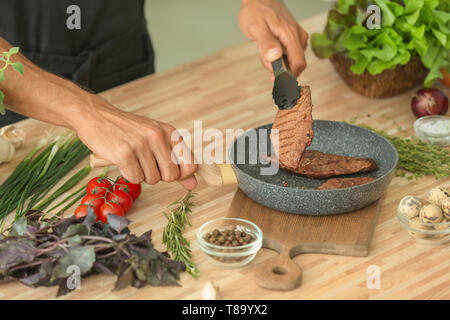 L'homme préparer de délicieux plats de viande avec des épices en cuisine Banque D'Images