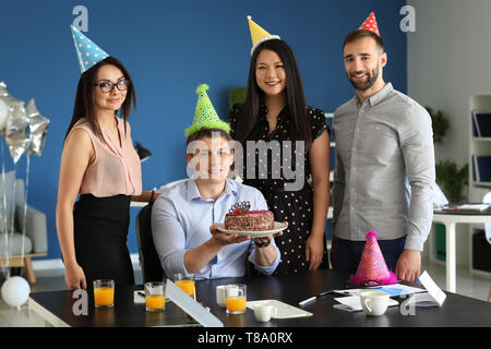 Jeune homme avec gâteau d'anniversaire et ses collègues de parti au pouvoir Banque D'Images