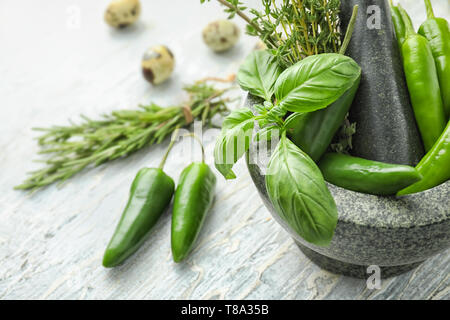 Mortier avec des piments frais et d'herbes sur fond clair Banque D'Images