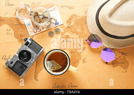 La composition avec appareil photo, chapeau, lunettes, tasse de thé et de l'argent sur vintage carte du monde. Concept de planification de voyage Banque D'Images