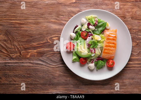 Plaque avec de délicieux poissons grillés et salade fraîche sur table en bois Banque D'Images