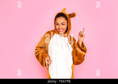 Jeune femme en bunny kigurumi active danse isolé sur fond rose à la joyeuse souriante de l'appareil photo Banque D'Images