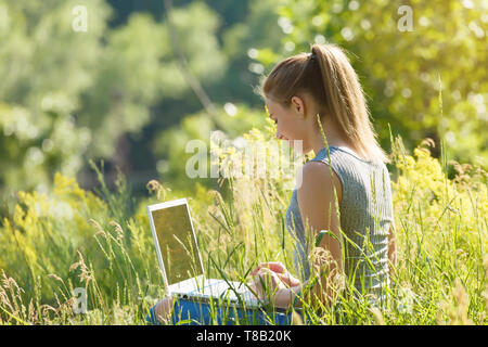 Une fille avec un ordinateur portable dans la nature parmi l'herbe verte. Fille avec coffre à l'extérieur à la recherche à l'écran Banque D'Images