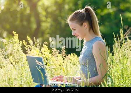 Une fille avec un ordinateur portable dans la nature parmi l'herbe verte. Fille avec coffre à l'extérieur à la recherche à l'écran Banque D'Images