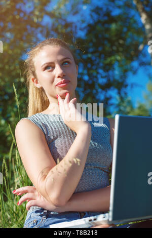 Une fille avec un ordinateur portable dans la nature parmi l'herbe verte. Fille avec coffre à l'extérieur à la recherche à l'écran Banque D'Images