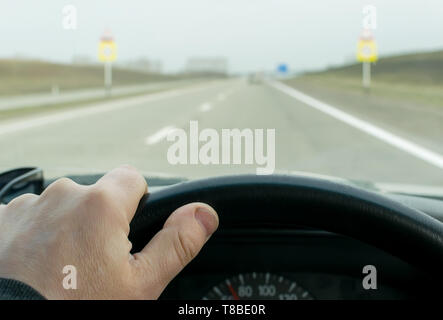 Vue de la main du conducteur sur le volant de la voiture qui est sur la route Banque D'Images