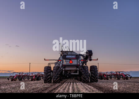 Swift Current, SK/Canada - Mai 10, 2019 : Coucher de soleil sur tracteur Caterpillar et Bourgault du matériel d'ensemencement dans le domaine de la Saskatchewan, Canada Banque D'Images
