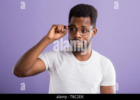 L'Afrique dans les verres joyeux gars habillé en blanc t shirt smiling ayant bonne humeur de toucher le menton tout en se posant en studio sur fond violet. Soins du visage Banque D'Images