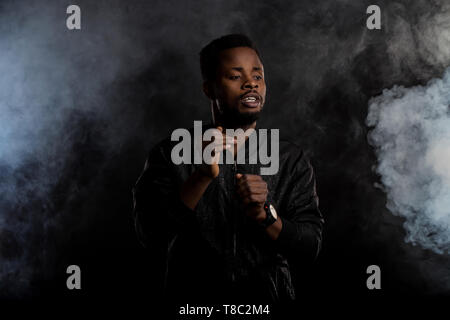Jusqu'à la taille de balle beau confident young african american man in black veste avec des gestes de barbe de la danse, élever les mains en l'air, à côté de seri Banque D'Images