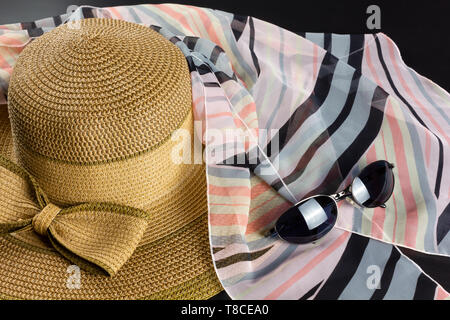 Chapeau de paille avec un grand arc, un foulard rose et noir et une paire de lunettes de soleil Banque D'Images
