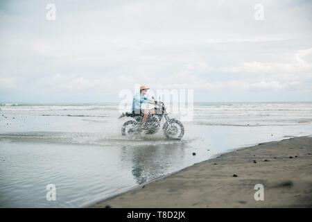 L'homme à la moto d'équitation sur la plage. Moto cross dirtbiker sur la plage coucher de soleil sur Bali. Les jeunes hommes hipster jouissant de la liberté et de vie actif, ayant Banque D'Images