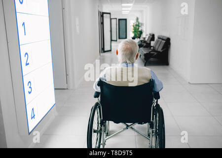 Lonely man in wheelchair assis devant le couloir de l'hôpital, vue de dos. Banque D'Images