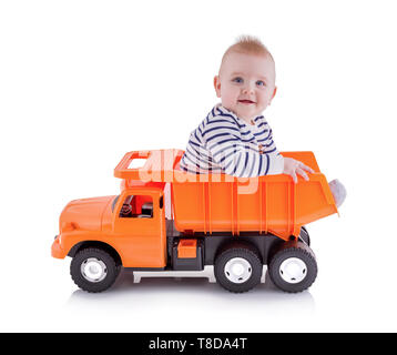 Happy Young boy sitting in open-box lit de camion benne jouet, isolé sur fond blanc avec ombre de réflexion. Tout-petit se trouve sur un camion dumper. Ador Banque D'Images